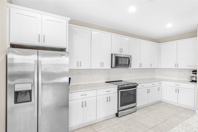 kitchen featuring backsplash, light tile patterned floors, light stone counters, white cabinetry, and stainless steel appliances