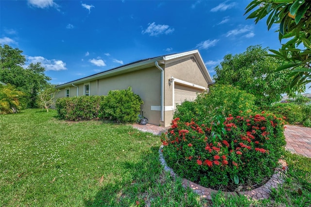 view of side of property featuring a garage, a lawn, and stucco siding