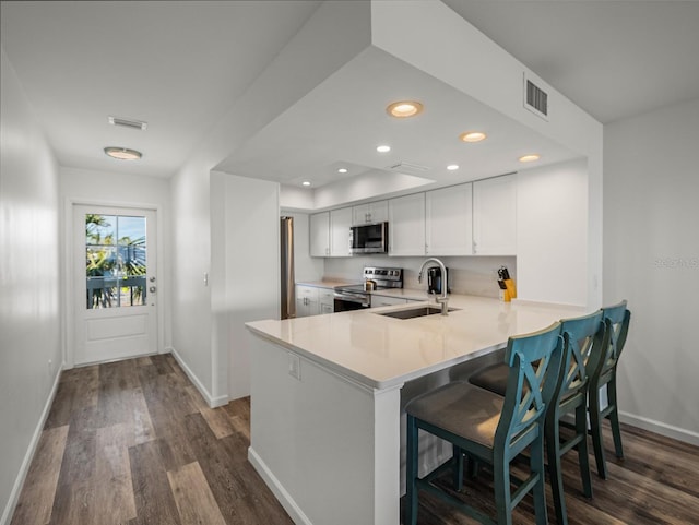 kitchen featuring a kitchen bar, sink, appliances with stainless steel finishes, kitchen peninsula, and white cabinets