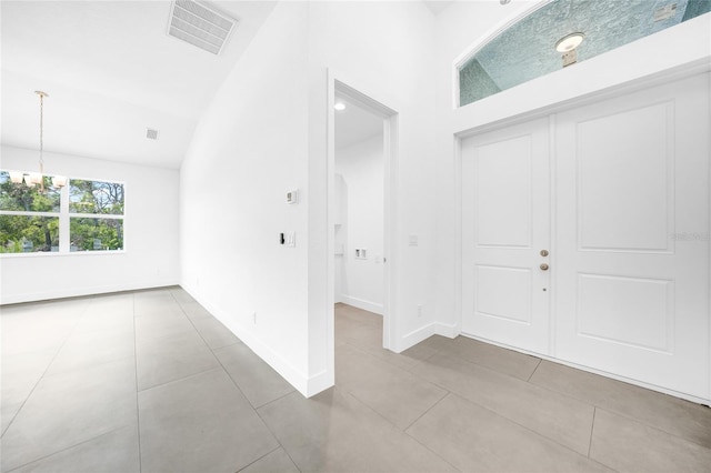 foyer entrance with lofted ceiling, light tile patterned floors, a chandelier, visible vents, and baseboards