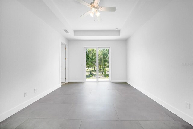 tiled spare room featuring a raised ceiling and ceiling fan