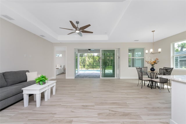 living room featuring ceiling fan with notable chandelier and a raised ceiling