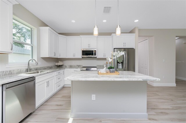 kitchen featuring light stone counters, a center island, sink, appliances with stainless steel finishes, and white cabinets