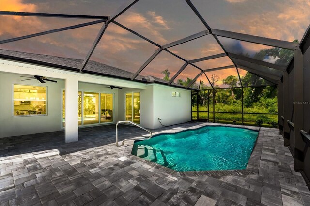 pool at dusk featuring ceiling fan, a patio area, and glass enclosure