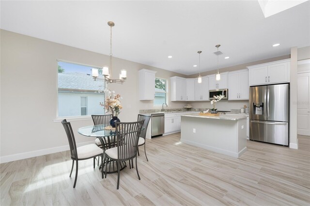 kitchen with decorative light fixtures, appliances with stainless steel finishes, a kitchen island, and white cabinetry