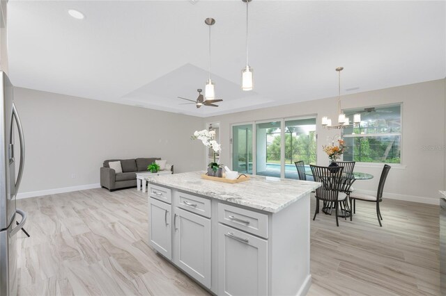 kitchen featuring stainless steel refrigerator, ceiling fan with notable chandelier, decorative light fixtures, light stone counters, and a kitchen island