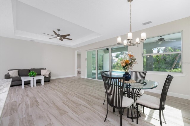 dining area featuring ceiling fan with notable chandelier, a raised ceiling, and light hardwood / wood-style floors