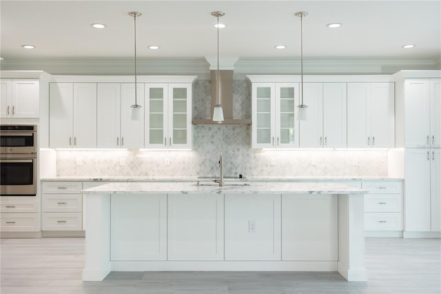 kitchen with white cabinets, stainless steel double oven, a center island with sink, and decorative backsplash