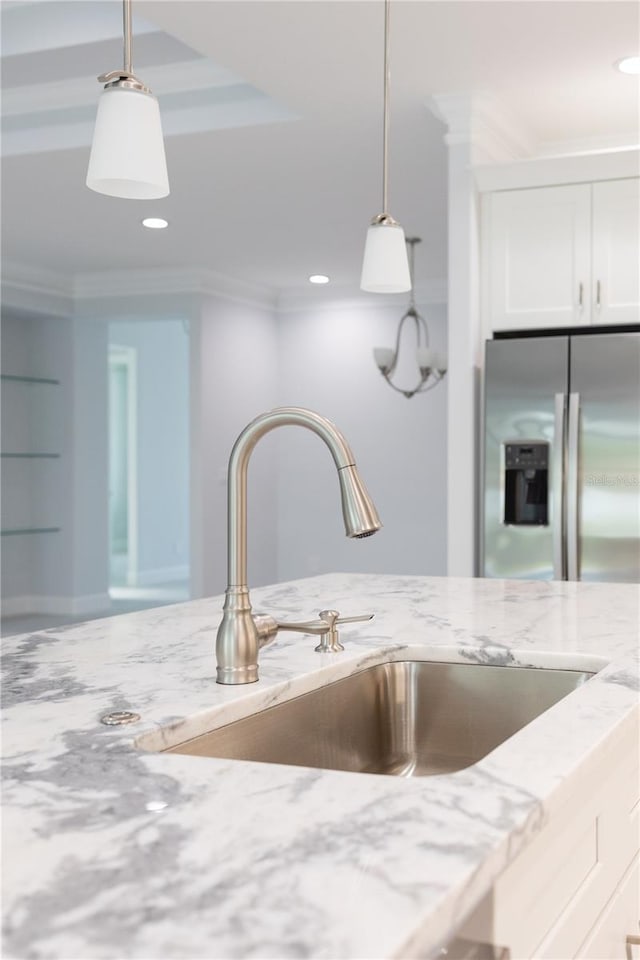 kitchen featuring light stone counters, white cabinetry, sink, stainless steel fridge, and ornamental molding