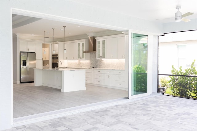 kitchen with wall chimney exhaust hood, a center island with sink, light hardwood / wood-style flooring, hanging light fixtures, and stainless steel appliances