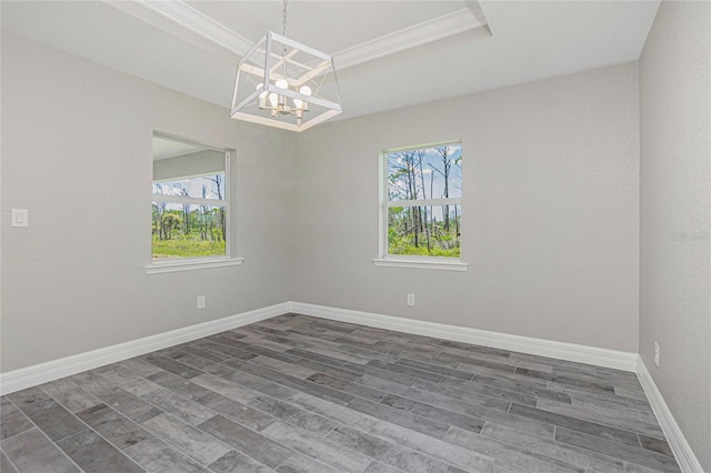 spare room with wood finished floors, baseboards, an inviting chandelier, a tray ceiling, and ornamental molding