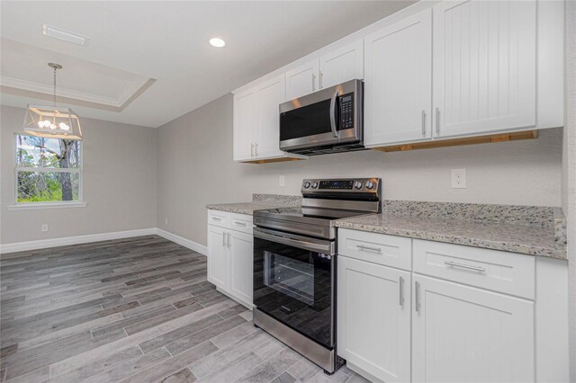 kitchen with light hardwood / wood-style flooring, appliances with stainless steel finishes, a tray ceiling, crown molding, and white cabinetry