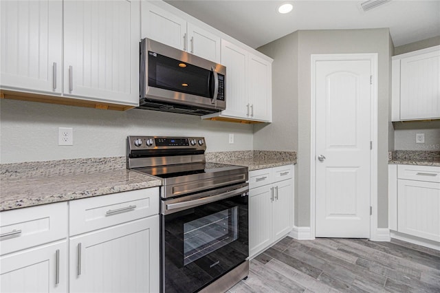 kitchen featuring light wood-type flooring, light stone counters, recessed lighting, stainless steel appliances, and white cabinetry