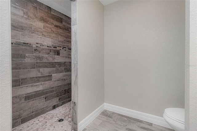 full bathroom with a tile shower, toilet, baseboards, and wood finished floors