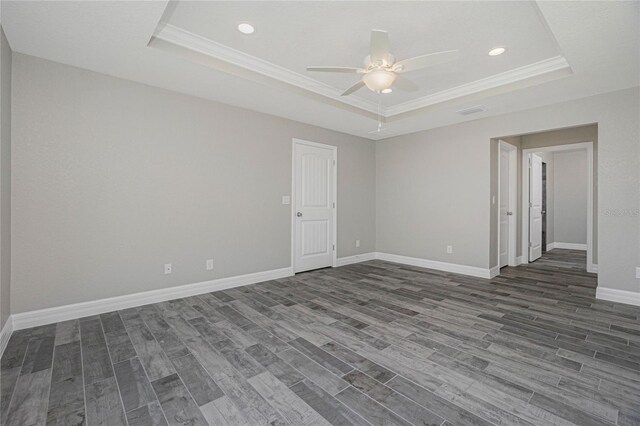 empty room with dark wood-type flooring, ceiling fan, a raised ceiling, and ornamental molding