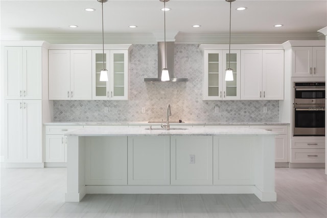 kitchen with backsplash, sink, wall chimney exhaust hood, pendant lighting, and a kitchen island with sink