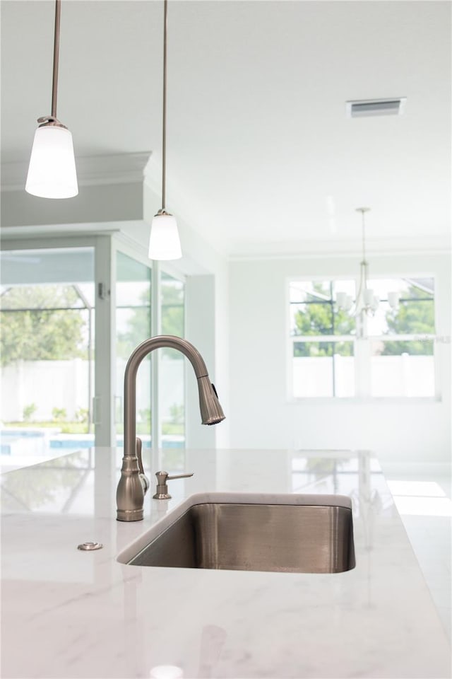 room details with an inviting chandelier, light stone countertops, pendant lighting, ornamental molding, and sink