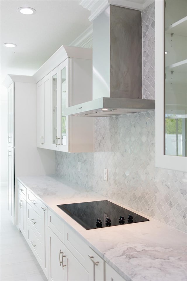 kitchen featuring backsplash, black electric stovetop, wall chimney range hood, and white cabinets