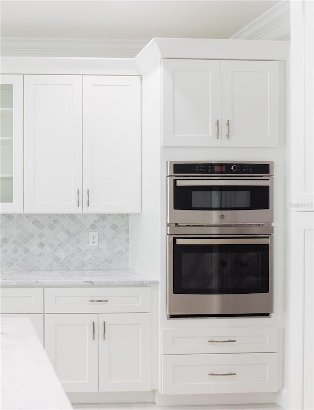 kitchen with stainless steel double oven, light stone counters, backsplash, and white cabinets