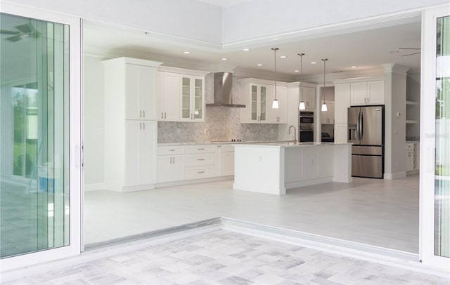 kitchen with stainless steel fridge, a kitchen island with sink, light hardwood / wood-style floors, hanging light fixtures, and wall chimney range hood