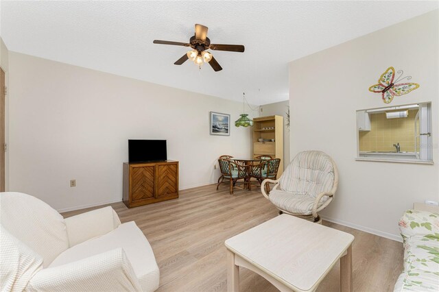 living room featuring light hardwood / wood-style flooring, ceiling fan, and a textured ceiling