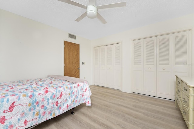 bedroom featuring light wood-type flooring, ceiling fan, a textured ceiling, and two closets