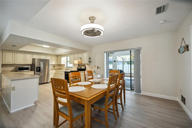 dining area with light wood-type flooring, sink, a raised ceiling, and a textured ceiling