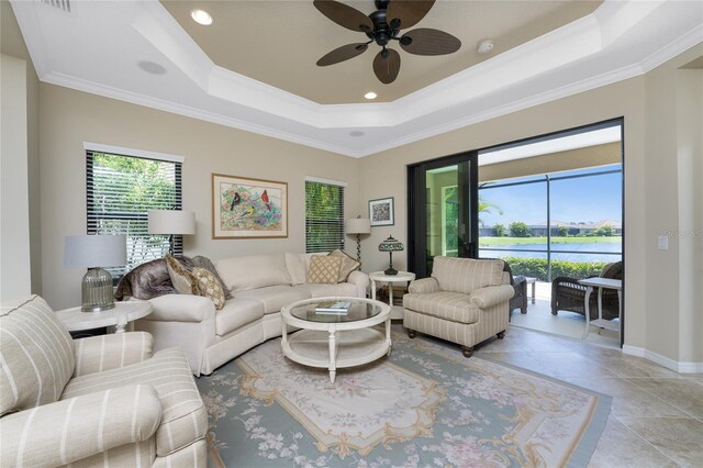 living room featuring crown molding, a raised ceiling, a water view, and ceiling fan