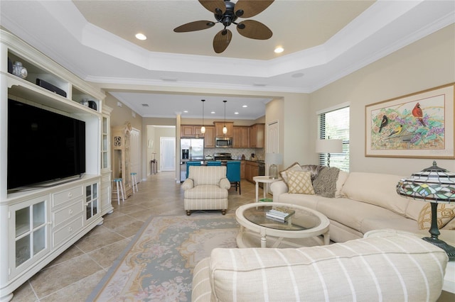 living area featuring a tray ceiling, crown molding, light tile patterned floors, recessed lighting, and ceiling fan