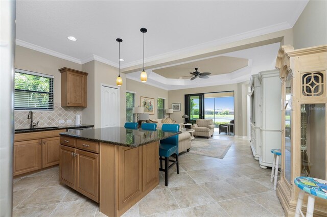 kitchen with dark stone counters, a center island, sink, ceiling fan, and a raised ceiling