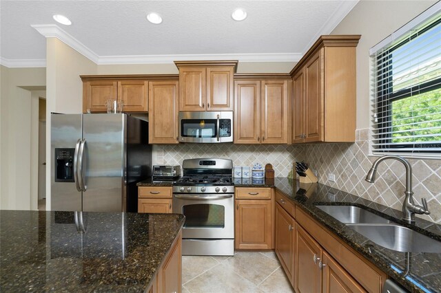 kitchen featuring dark stone countertops, light tile patterned floors, appliances with stainless steel finishes, sink, and ornamental molding