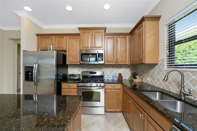 kitchen featuring ornamental molding, brown cabinets, dark stone countertops, stainless steel appliances, and a sink