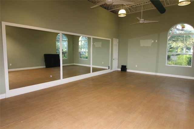 empty room with a high ceiling, baseboards, a ceiling fan, and wood finished floors