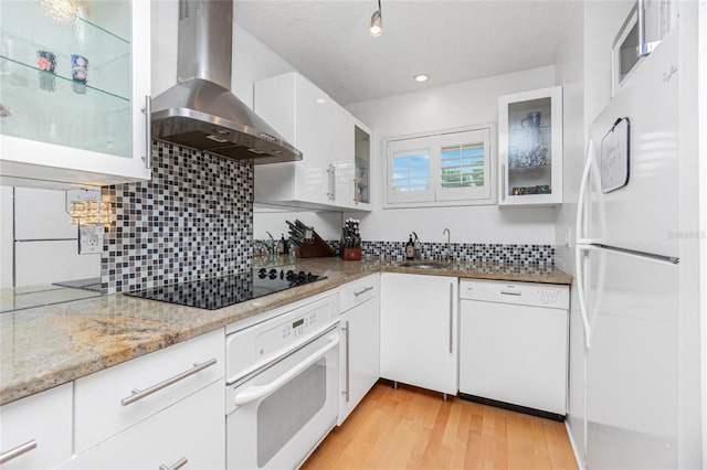 kitchen featuring white cabinetry, sink, wall chimney range hood, light stone counters, and white appliances