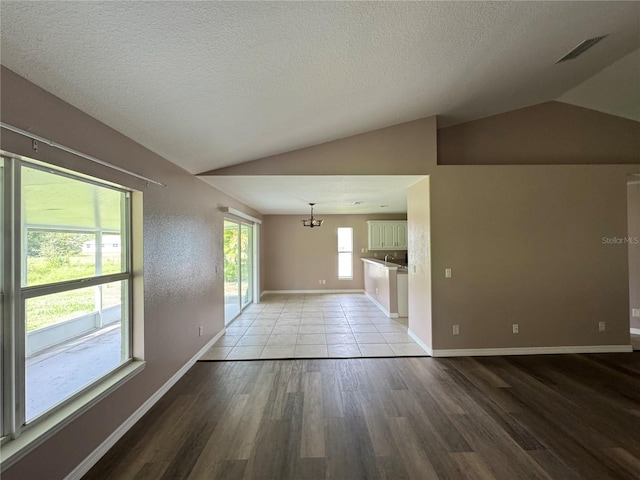 unfurnished living room featuring lofted ceiling, a chandelier, a textured ceiling, and light hardwood / wood-style floors