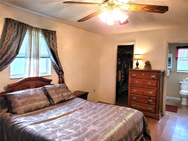 bedroom with a textured ceiling, a walk in closet, a closet, ensuite bathroom, and ceiling fan