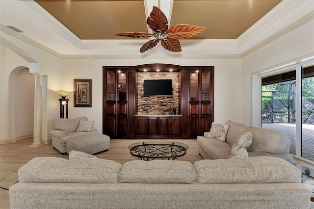 living room with light wood-type flooring, ornate columns, a tray ceiling, ceiling fan, and ornamental molding