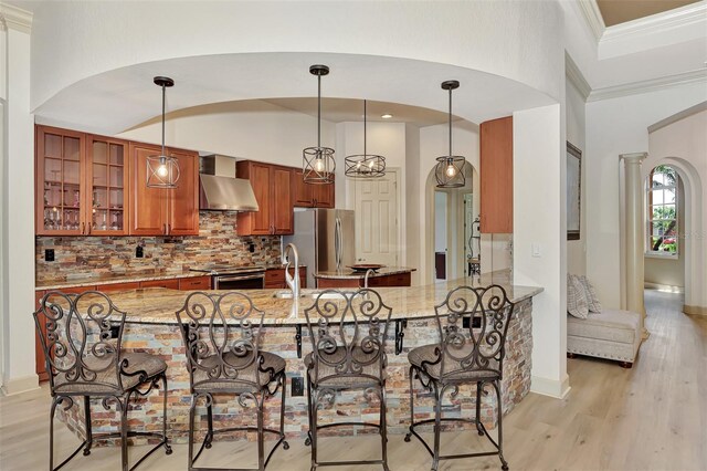 kitchen featuring tasteful backsplash, light stone counters, wall chimney exhaust hood, and kitchen peninsula