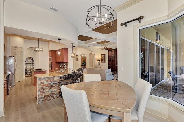 dining room with coffered ceiling, ceiling fan with notable chandelier, beamed ceiling, and light hardwood / wood-style flooring