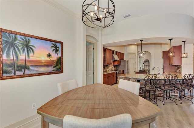 dining room featuring light wood-type flooring, crown molding, and a notable chandelier