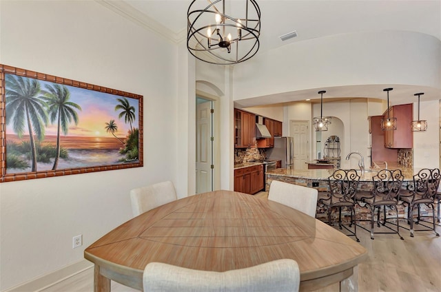 dining space featuring light wood-type flooring, visible vents, ornamental molding, arched walkways, and a chandelier