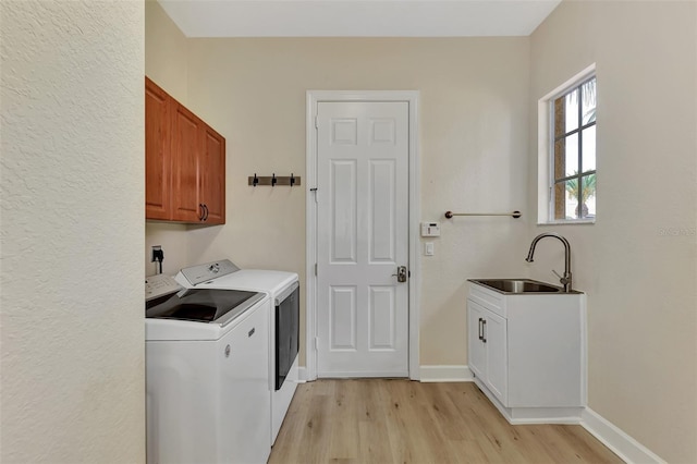 laundry room featuring baseboards, light wood-style flooring, washer and dryer, cabinet space, and a sink