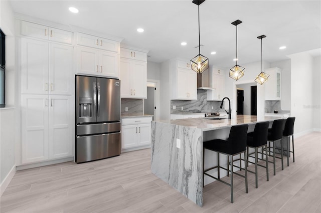 kitchen featuring light stone countertops, stainless steel refrigerator with ice dispenser, white cabinetry, and hanging light fixtures