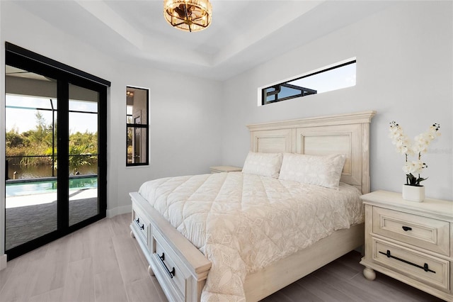 bedroom featuring access to outside, a raised ceiling, and light wood-type flooring