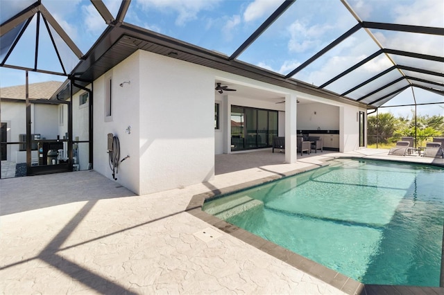 view of swimming pool with glass enclosure, ceiling fan, and a patio area