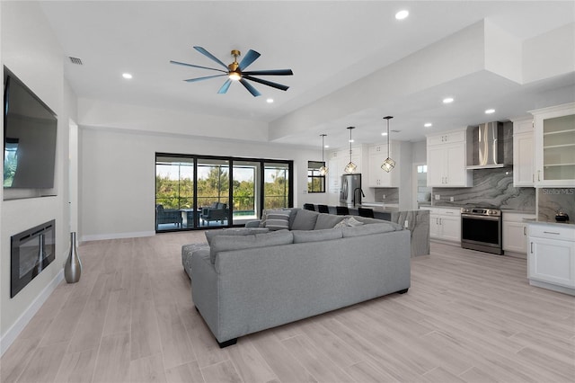 living room featuring recessed lighting, light wood-style flooring, a ceiling fan, a glass covered fireplace, and baseboards