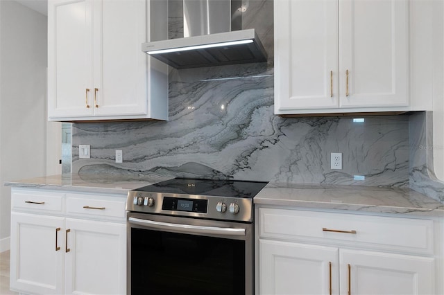 kitchen featuring wall chimney exhaust hood, light stone counters, stainless steel electric range, white cabinetry, and backsplash