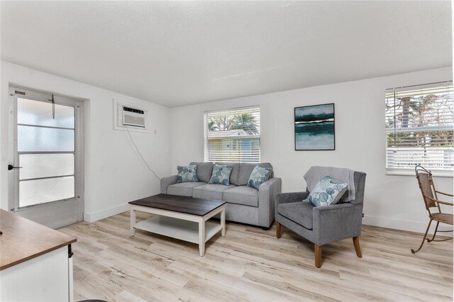 living area featuring light wood-style flooring, an AC wall unit, and baseboards