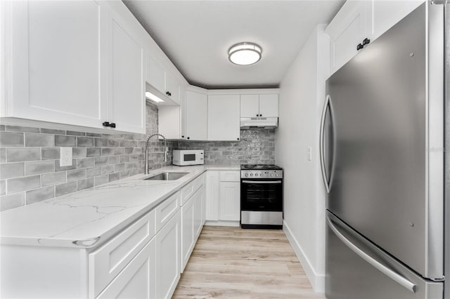 kitchen featuring white cabinets, under cabinet range hood, light wood-type flooring, decorative backsplash, and appliances with stainless steel finishes