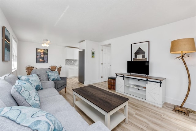 living room with light wood finished floors, a ceiling fan, and baseboards